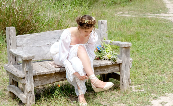A woman in a white dress sitting on a rustic bench outdoors.