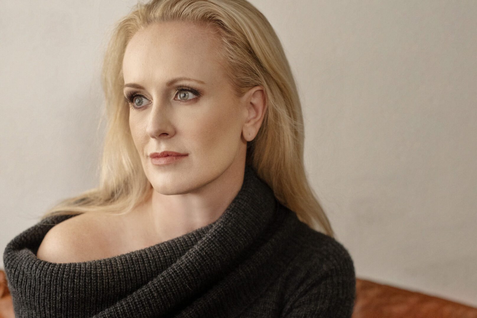 Thoughtful woman with blonde hair gazing to the side in a cozy dark sweater.