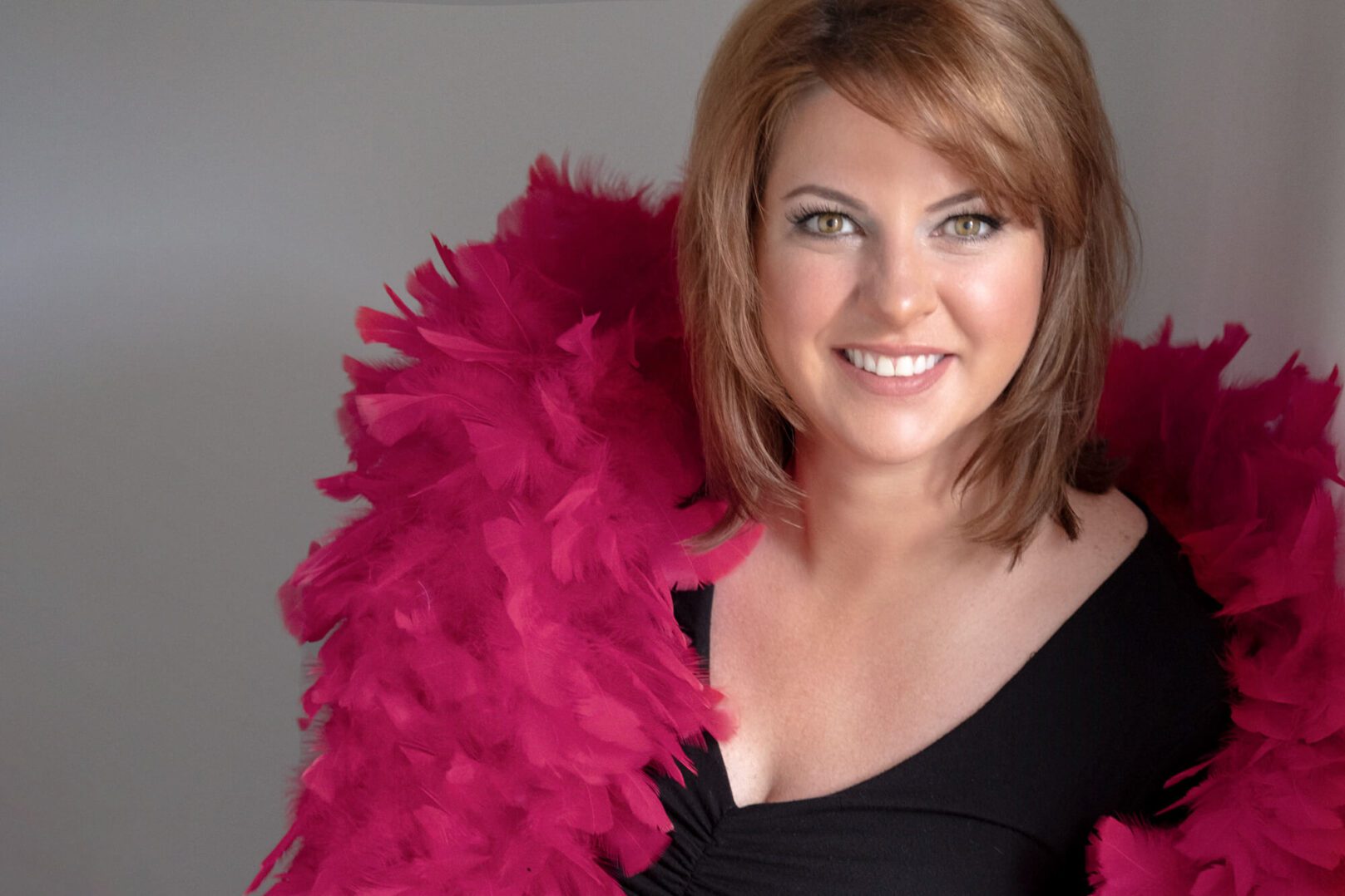 Smiling woman with a vibrant pink feather boa and a black top.