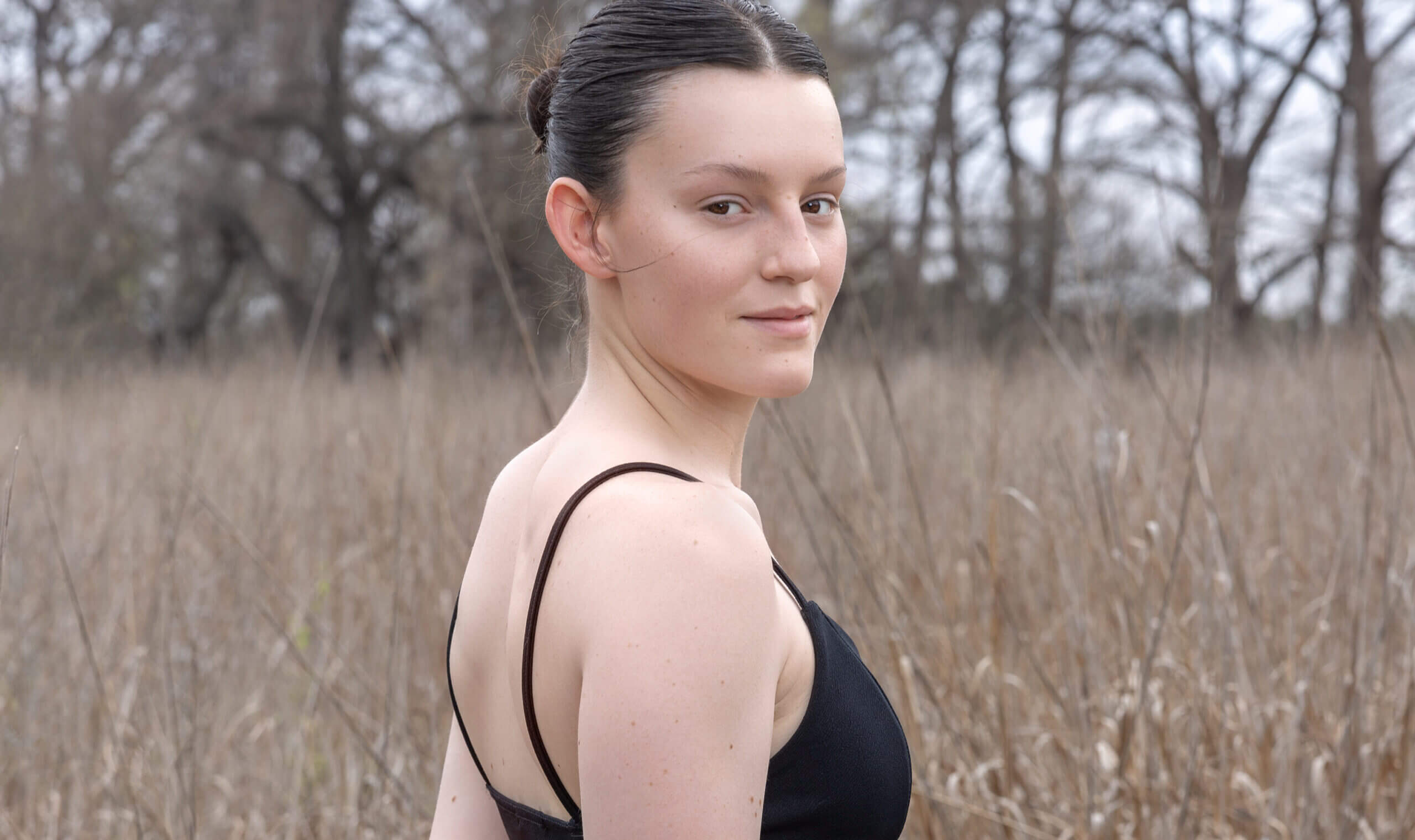 Young woman in a black tank top outdoors with a natural background.